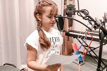 zdjęcie dziewczynka w studio nagraniowym śpiewa do mikrofonu czytając z kartki