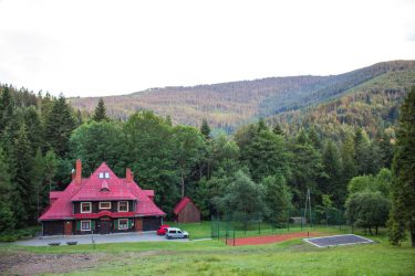 Ośrodek Górski Kordon z zewnątrz, drewniany dom z czerwonym dachem pośrodku lasu